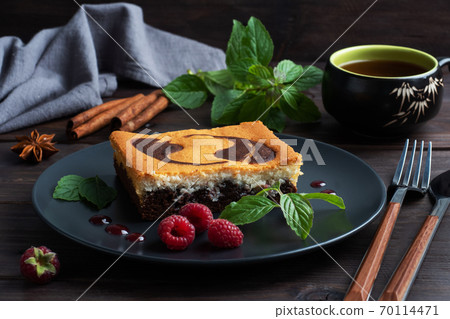 A piece of double-layer cake on a plate of chocolate brownies and curd cheesecake with raspberries. Dark background copy space A piece of double-layer cake on a plate of chocolate brownies and curd cheesecake with raspberries. Dark background copy space 70114471