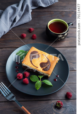 A piece of double-layer cake on a plate of chocolate brownies and curd cheesecake with raspberries. Dark background copy space A piece of double-layer cake on a plate of chocolate brownies and curd cheesecake with raspberries. Dark background copy space 70114477