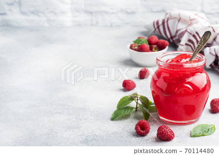 Homemade raspberry jam in a glass jar and fresh raspberries with mint on a grey concrete background. Copy space Homemade raspberry jam in a glass jar and fresh raspberries with mint on a grey concrete background. Copy space 70114480