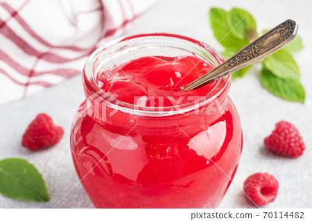 Homemade raspberry jam in a glass jar and fresh raspberries with mint on a grey concrete background. Copy space Homemade raspberry jam in a glass jar and fresh raspberries with mint on a grey concrete background. Copy space 70114482