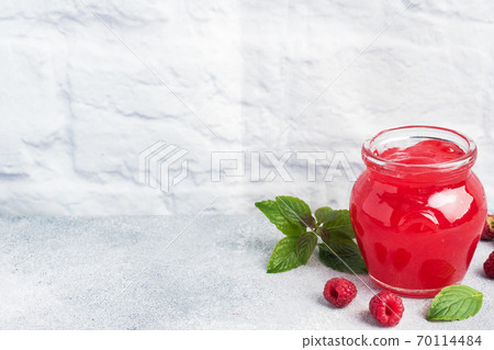 Homemade raspberry jam in a glass jar and fresh raspberries with mint on a grey concrete background. Copy space Homemade raspberry jam in a glass jar and fresh raspberries with mint on a grey concrete background. Copy space 70114484