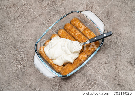 tiramisu dessert cooking - Traditional Italian Savoiardi ladyfingers Biscuits and cream in glass baking dish on concrete background tiramisu dessert cooking - Traditional Italian Savoiardi ladyfingers Biscuits and cream in glass baking dish on concrete background 70116029
