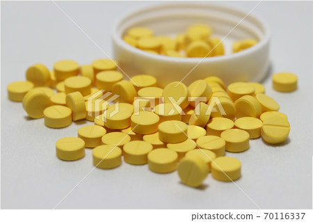 Pile of yellow round medicine on the white floor and white plastic cap. Pile of yellow round medicine on the white floor and white plastic cap. 70116337