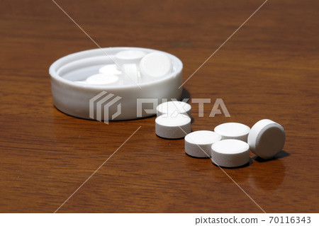 Pile of white round medicine on the wooden floor and white plastic cap. 70116343