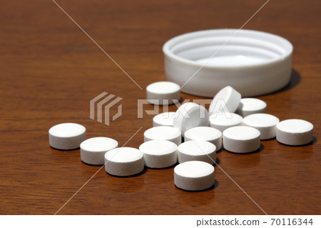 Pile of white round medicine on the wooden floor and white plastic cap. Pile of white round medicine on the wooden floor and white plastic cap. 70116344