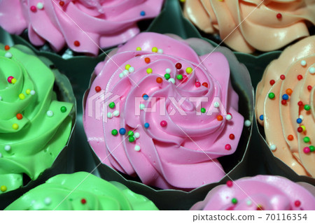 Pink, green and orange color of cup cake with colorful rounded sugar beads on the cream. Pink, green and orange color of cup cake with colorful rounded sugar beads on the cream. 70116354