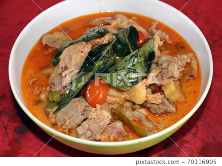 Chicken Curry with basil, tomato and turkey berry in the bowl on the red wooden table. Chicken Curry with basil, tomato and turkey berry in the bowl on the red wooden table. 70116905