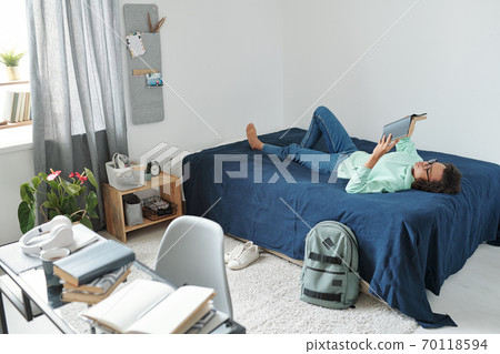 Young mixed-race female student holding open book in front of face while reading Young mixed-race female student holding open book in front of face while reading 70118594