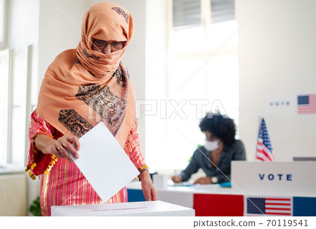 Islamic woman voter putting her vote in the ballot box, usa elections and coronavirus. 70119541