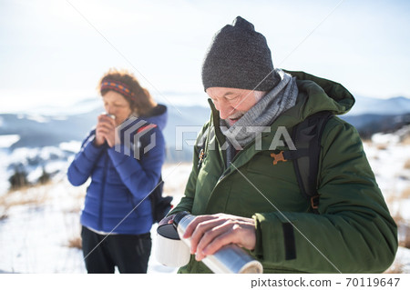 Senior couple hikers in snow-covered winter nature, drinking hot tea. Senior couple hikers in snow-covered winter nature, drinking hot tea. 70119647