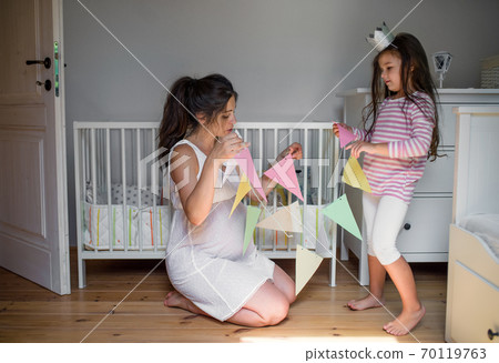 Portrait of pregnant woman with small daughter indoors at home, decorating bedroom. 70119763