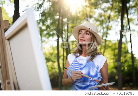 Portrait of mature woman with pallete painting outdoors in garden. 70119795