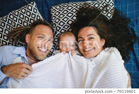 Young couple with baby daughter resting under blanket, looking at camera. Young couple with baby daughter resting under blanket, looking at camera. 70119801