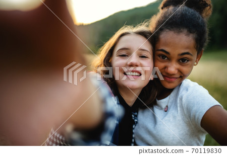 Front view of young teenager girls friends outdoors in nature, taking selfie. 70119830