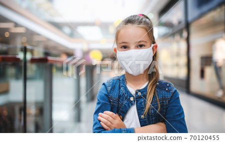 Small girl with face mask looking at camera indoors in shopping center, coronavirus concept. Small girl with face mask looking at camera indoors in shopping center, coronavirus concept. 70120455