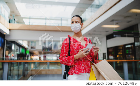 Woman with face mask standing with smartphone indoors in shopping center, coronavirus concept. Woman with face mask standing with smartphone indoors in shopping center, coronavirus concept. 70120489