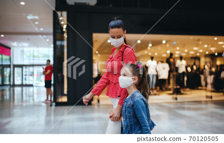 Mother and daughter with face mask indoors in shopping center, coronavirus concept. Mother and daughter with face mask indoors in shopping center, coronavirus concept. 70120505