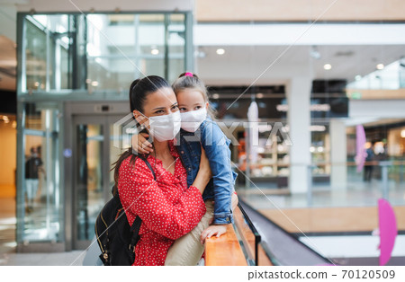 Mother and daughter with face mask standing indoors in shopping center, coronavirus concept. Mother and daughter with face mask standing indoors in shopping center, coronavirus concept. 70120509
