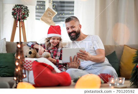 Father with small daughter indoors at home at Christmas, using tablet. Father with small daughter indoors at home at Christmas, using tablet. 70120592