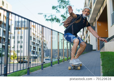 Portrait of mature man riding skateboard outdoors in city, going back to work. Portrait of mature man riding skateboard outdoors in city, going back to work. 70120616