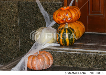 Spooky Halloween pumpkin jack-o-lanterns with spider web on the steps at a door. Decorations for Halloween holiday Spooky Halloween pumpkin jack-o-lanterns with spider web on the steps at a door. Decorations for Halloween holiday 70120816