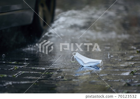 Used face mask in puddle during rain 70123532