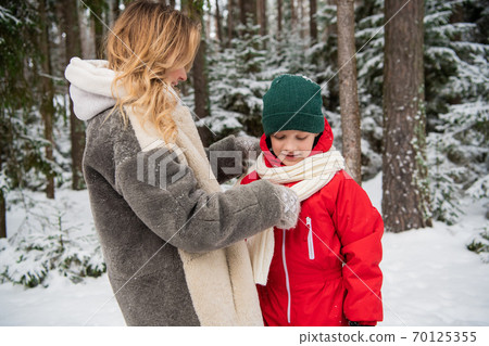 A young mother adjusts her son's scarf on a frosty morning in the woods A young mother adjusts her son's scarf on a frosty morning in the woods 70125355