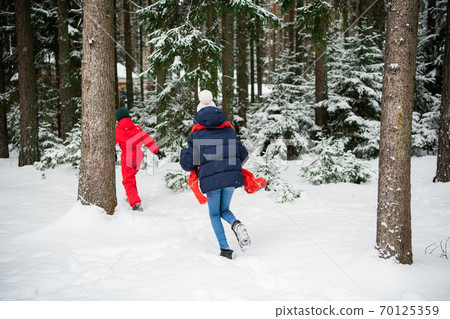 Girl and boy in winter clothes running in winter snow forest, back view 70125359
