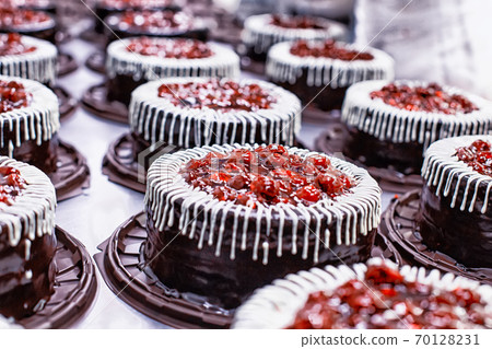 Many beautiful and delicious chocolate cakes with fresh cherry and cream. Confectionery production for the manufacture of cakes and pastries, torte, background 70128231