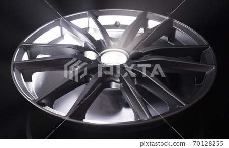 Modern beautiful car alloy wheel in the form of rays that is highlighted by rays of light and sparkle, black background Modern beautiful car alloy wheel in the form of rays that is highlighted by rays of light and sparkle, black background 70128255