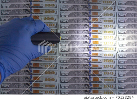 An expert checks American money dollars for counterfeiting with an ultraviolet flashlight. The concept of detention and counterfeiting, copy space for text An expert checks American money dollars for counterfeiting with an ultraviolet flashlight. The concept of detention and counterfeiting, copy space for text 70128294