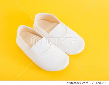White gym shoes for children on a yellow background. Concepts for comfortable and light indoor shoes and sports, ballet shoes 70128356