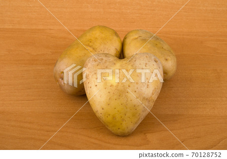 Potatoes on a wooden table. One of them is in the form of a heart. Potatoes on a wooden table. One of them is in the form of a heart. 70128752
