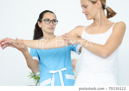 Woman doctor physiotherapist holds hand to woman patient in white clothes portrait 70130122