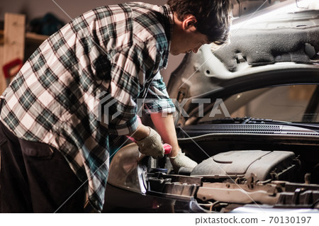 a young male car mechanic in a shirt and gloves checks the engine oil level in a black car. a young male car mechanic in a shirt and gloves checks the engine oil level in a black car. 70130197
