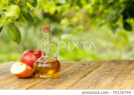 Apple vinegar in glass bottle and fresh red apples on wooden boards Apple vinegar in glass bottle and fresh red apples on wooden boards 70130749