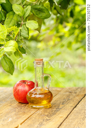 Apple vinegar in glass bottle and fresh red apple on wooden boards Apple vinegar in glass bottle and fresh red apple on wooden boards 70130752