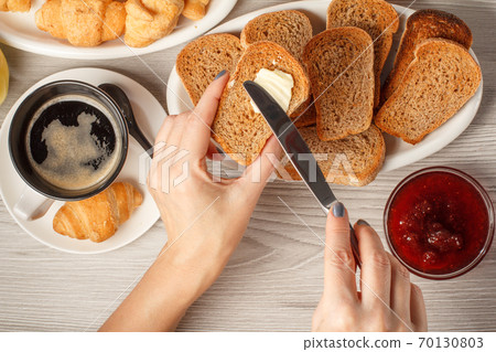 Female hands spreading butter on toast with cup of black coffee 70130803
