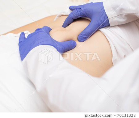 Doctor surgeon examines the stomach of a girl patient for the presence of umbilical hernia. Abdominal wall disease concept with umbilical hernia, reinforced hernia Doctor surgeon examines the stomach of a girl patient for the presence of umbilical hernia. Abdominal wall disease concept with umbilical hernia, reinforced hernia 70131328
