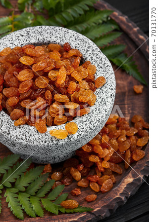 Close up of yellow raisins in a stone bowl, close up, dark background Close up of yellow raisins in a stone bowl, close up, dark background 70131770