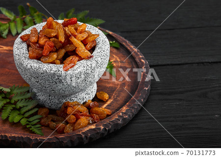 Close up of yellow raisins in a stone bowl, close up, dark background Close up of yellow raisins in a stone bowl, close up, dark background 70131773