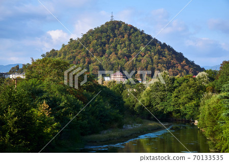 landscape with a hill, a river and a power transmission tower at the top landscape with a hill, a river and a power transmission tower at the top 70133535