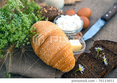 Organic food - milk, bread, eggs, cheese, butter, knife, lying on the table, against the background of a wheat field. 70133651