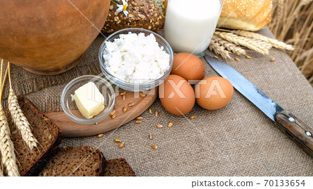 Organic food - milk, bread, eggs, cheese, butter, knife, lying on the table, against the background of a wheat field. 70133654