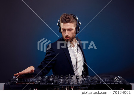 Man DJ in dark suit play music on a Dj's mixer. Studio shot. Dark blue background Man DJ in dark suit play music on a Dj's mixer. Studio shot. Dark blue background 70134001