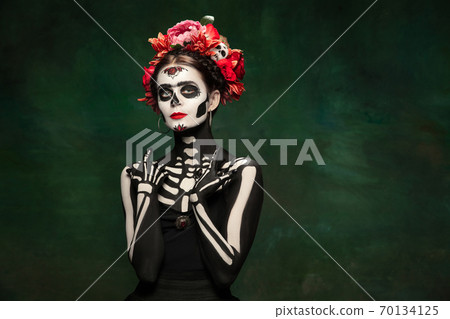 Young girl in the image of Santa Muerte, Saint death or Sugar skull with bright make-up. Portrait isolated on studio background. Young girl in the image of Santa Muerte, Saint death or Sugar skull with bright make-up. Portrait isolated on studio background. 70134125