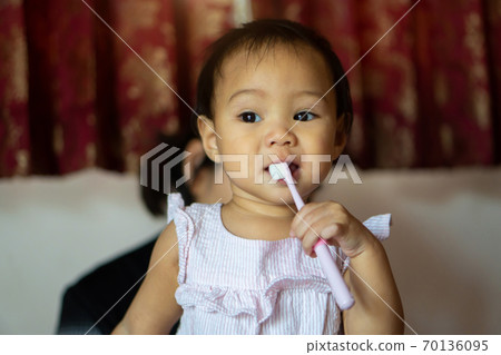11-month-old girl practicing a toothbrush by herself from her mother's teaching. 11-month-old girl practicing a toothbrush by herself from her mother's teaching. 70136095
