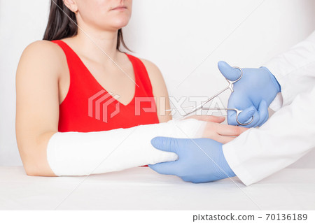 Doctor traumatologist removes the fixing bandage for a girl who has a tear and sprain on her arm, medical, ligament rupture Doctor traumatologist removes the fixing bandage for a girl who has a tear and sprain on her arm, medical, ligament rupture 70136189
