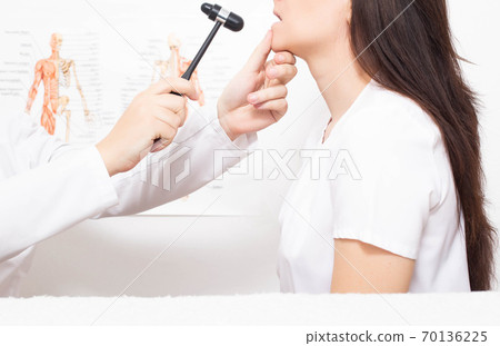 A neurologist doctor checks the mandibular reflex in a girl patient for the presence of neuropathology, pseudobulbar syndrome. A neurologist doctor checks the mandibular reflex in a girl patient for the presence of neuropathology, pseudobulbar syndrome. 70136225