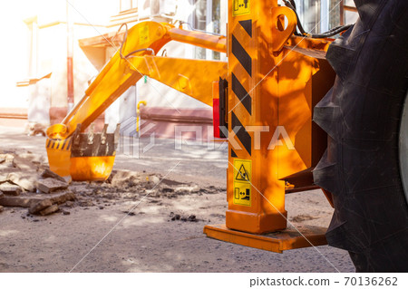 An excavator's rear bucket digs in the courtyard of a residential building. Laying gas and water supply, replacing old pipes, accident An excavator's rear bucket digs in the courtyard of a residential building. Laying gas and water supply, replacing old pipes, accident 70136262